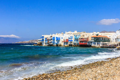 Buildings by sea against blue sky