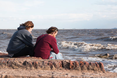 Couple sitting on shore at beach against sky