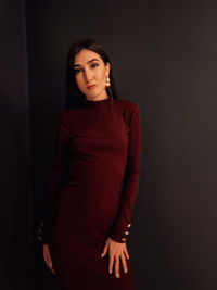 Portrait of young woman standing against black background