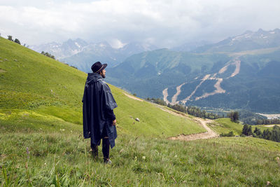 Man with a beard shepherd standing in the mountains in a black raincoat in the rain