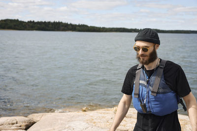 Man wearing life jacket standing on coast and looking away