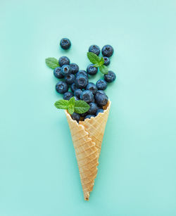 Ice cream cone filled with blueberries on the light green background