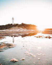 Lighthouse by sea against sky during sunset