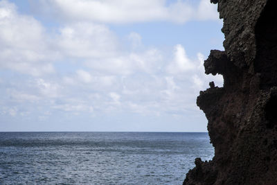 Rock formation by sea against cloudy sky