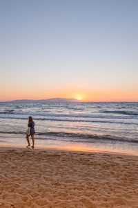 Rear view full length of woman walking on shore at beach during sunset