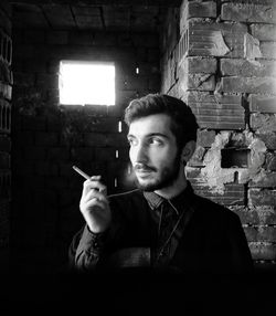 Portrait of young man holding cigarette against wall