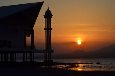 Silhouette building by sea against sky during sunset