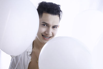 Portrait of smiling young man with balloons against white background