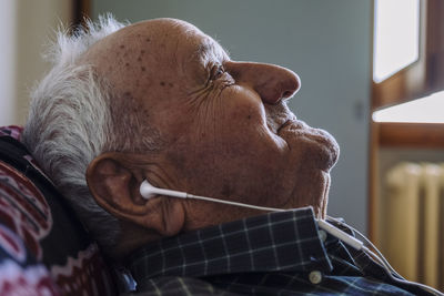 Close-up of thoughtful senior man listening music while relaxing on sofa at home