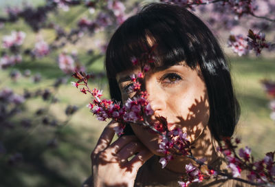 Portrait of woman with pink flowers against tree