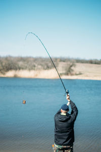 Rear view of man fishing in sea against sky