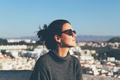 Young woman looking away in city against sky