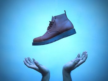 Cropped hand gesturing under shoes against blue background