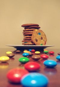 Surface level on multi colored candies by cookie stack on table against brown wall at home