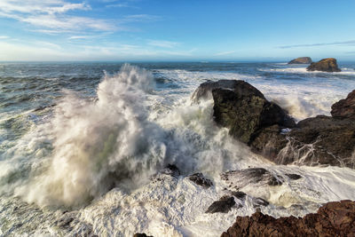 Waves splashing on rocks at shore against sky