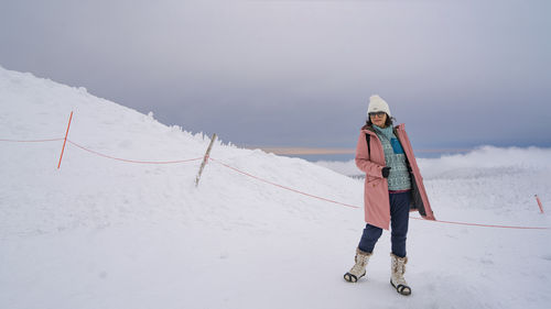 Full length of woman standing on snow covered field against clear sky