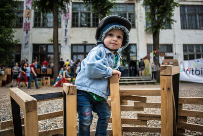 Portrait of boy wearing cap on wooden play equipment against building