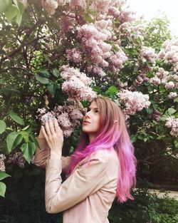 Young woman touching pink flowers blooming on tree