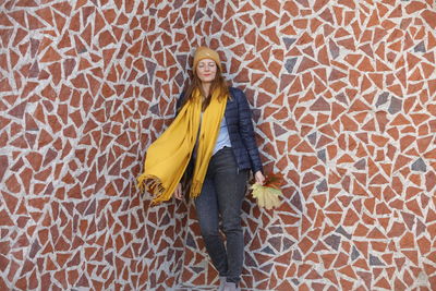 Full length portrait of woman standing against yellow wall