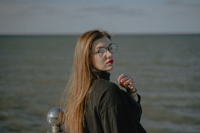 Portrait of young woman looking away against sea