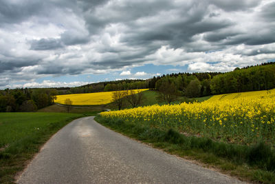 Country road amidst field against yellow sky
