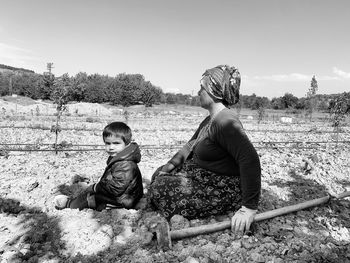 Portrait of woman farmer and her grandson sitting on field and taking a rest under hot weather.