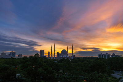 Scenic view of mosque by trees against cloudy sky during sunset