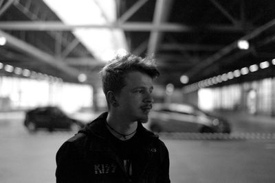 Portrait of young man standing against illuminated bridge at night