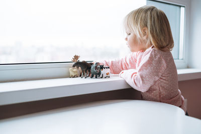 Side view of cute girl sitting on window