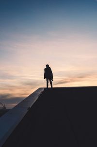 Rear view of silhouette man standing on building terrace against sky during sunset