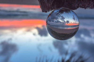 Close-up of crystal ball against sea during sunset