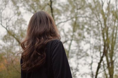 Rear view of woman standing against trees in forest