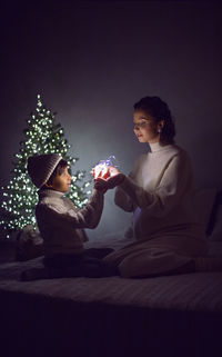 Mother and son in white knitted jumpers holding a garland. background of the tree on christmas