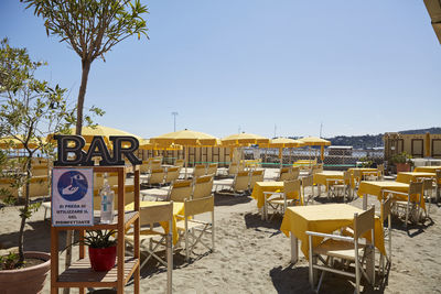 Chairs and tables on beach against clear sky