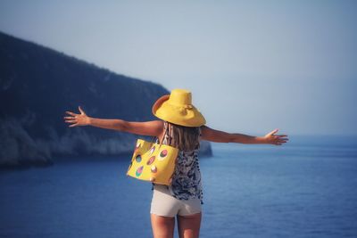 Rear view of woman with arms outstretched standing by sea