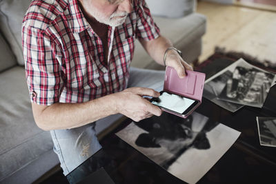 Midsection of senior man photographing old photograph through smart phone at home