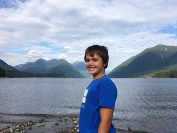 Portrait of smiling boy standing by lake against sky