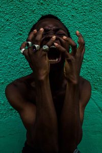 Angry shirtless young man screaming against painted wall