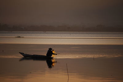 Silhouette man sitting in fishing boat on sea during sunset