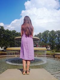 Rear view of girl standing at fountain on sunny day