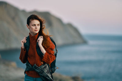 Portrait of young woman standing by sea against sky