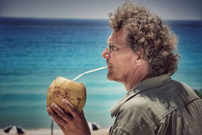 Mature man drinking coconut water against sea