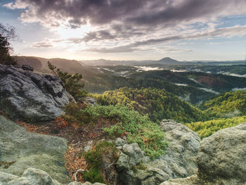 Sandstone rock with view into colorful mist in morning valley. blue daybreak sun hidden at horizon