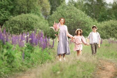 Happy caucasian family walking in lupine field with mother holding flowers