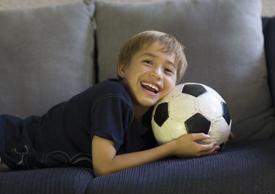 Portrait of boy with soccer ball lying on sofa at home