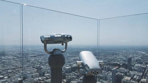 Coin-operated binoculars by glass against cityscape