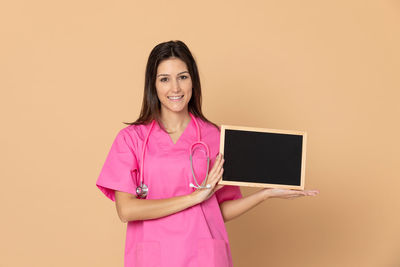 Portrait of a smiling young woman standing against pink background