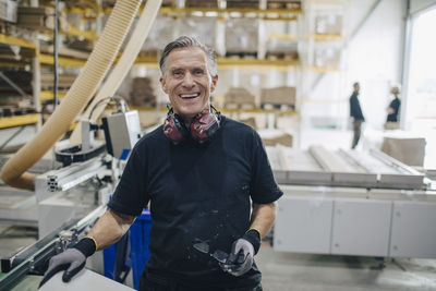 Portrait of smiling worker standing by machinery at lumber industry