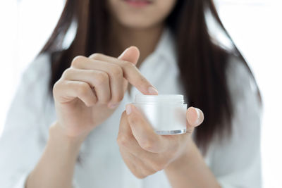 Midsection of woman holding moisturizer against white background