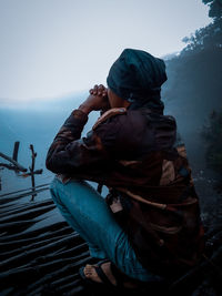 Rear view of man sitting on snow covered mountain against sky